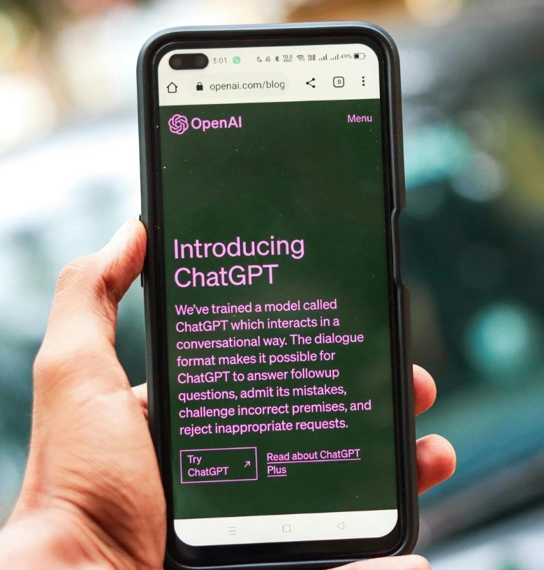 Persona usando un móvil con la web de OpenAI abierta, presentando ChatGPT como herramienta de inteligencia artificial generativa para conversaciones.